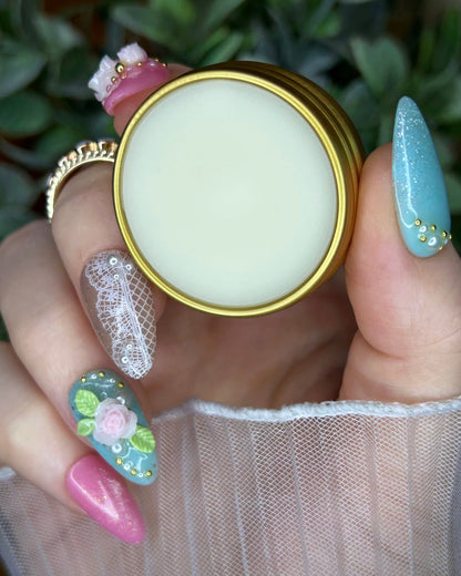 Hand holding a small round container with a gold lid against a blurred green background